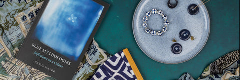 Blue Mythologies Reflections on a colour, blue earrings and assorted jewellery laid on top on a blue background and patterned scarf 