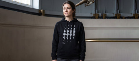 Person wearing a black hoodie with moon phase design in an observatory setting