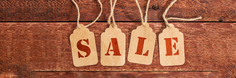 Four beige paper tags with red letters spelling 'SALE' on a wooden background