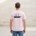 Man wearing a pink t-shirt with a ship design on the back, standing in a minimalistic room.