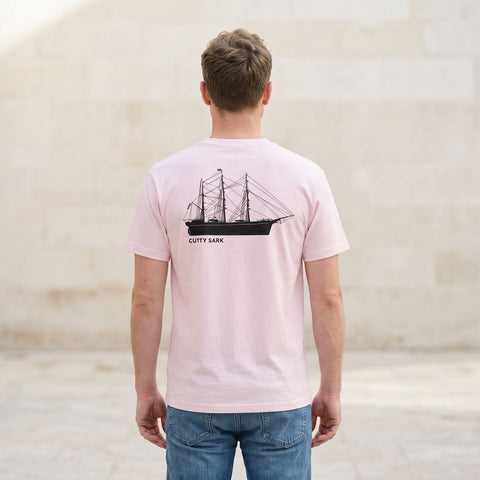 Man wearing a pink t-shirt with a ship design on the back, standing in a minimalistic room.
