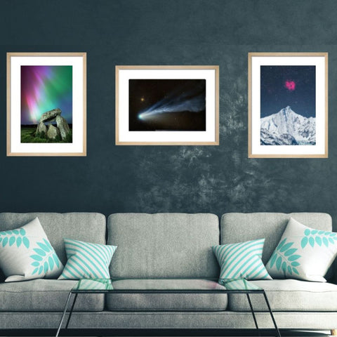 Framed space-themed artworks on a dark wall above a gray sofa with decorative pillows.