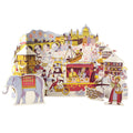 A colorful 3D pop-up cardboar Advent Calendar depicting a winter fair scene with a snowman, an elephant carrying a sign that reads 'FROST RAYE', a carousel, market stalls, and whimsical characters