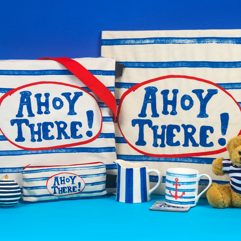 Blue and white striped tote bag, tea towel, cups, and pencil case with Ahoy! There branding in a red circle, against a blue background 