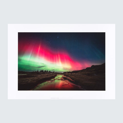 An art print featuring a landscape photograph of the vibrant aurora borealis over a dark valley with a reflective stream