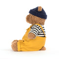 Teddy bear wearing a yellow dungarees, striped shirt, and navy hat 
