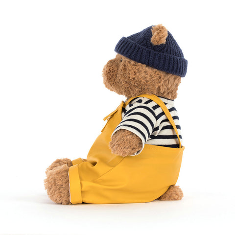 Teddy bear wearing a yellow dungarees, striped shirt, and navy hat 