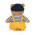 Teddy bear wearing a navy hat, striped shirt, and yellow overalls on a white background