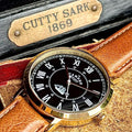 Watch with gold case and black dial on a leather strap, branded 'Cutty Sark'.