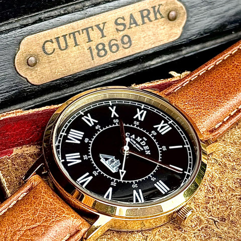 Watch with gold case and black dial on a leather strap, branded 'Cutty Sark'.