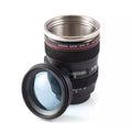 A novelty camera lens travel mug with a stainless steel interior and a black exterior designed to look like a Canon zoom lens, featuring a detached front lens piece on a white background.