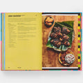 Open book showing a recipe for jerk chicken with a photograph of the dish on a wooden surface.