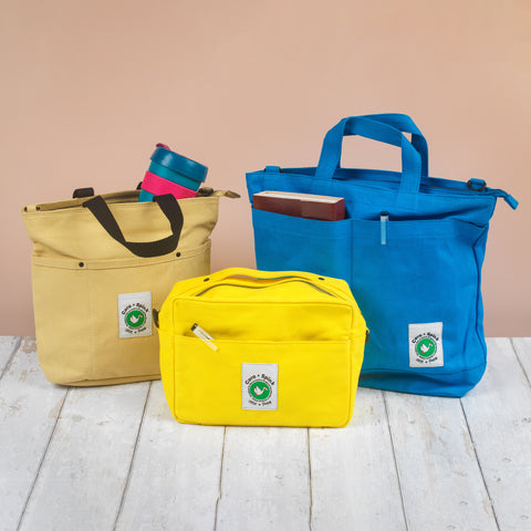 Three colorful bags (yellow, blue, and beige) with a visible brand logo on a wooden surface.