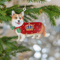 A Christmas ornament shaped like a Corgi dog wearing a red robe with a gold crown, hanging from a green Christmas tree branch.