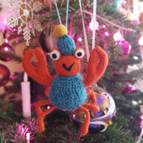 Knitted crab ornament hanging on a Christmas tree with colorful lights.