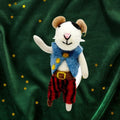Felt decoration of a mouse in a blue vest and red trousers on a green fabric background with gold stars.
