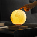 A glowing 3D Earth globe lamp floating above a wooden base on a dark table, with a person's hand touching the top of the lamp.