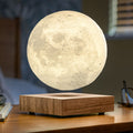 A glowing moon-shaped night light floating above a square wooden base on a wooden table, with a softly blurred bedroom background.
