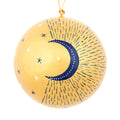 A spherical gold ornament hand decorated with a navy blue crescent moon, small white stars, and dotted line patterns