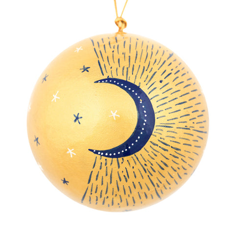 A spherical gold ornament hand decorated with a navy blue crescent moon, small white stars, and dotted line patterns
