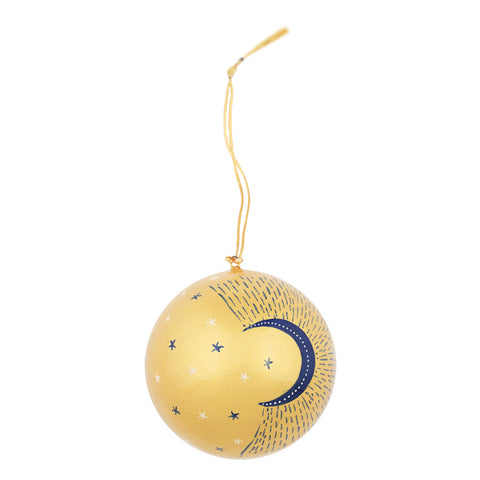 A spherical gold ornament decorated with a navy blue crescent moon, small white stars, and dotted line patterns, hanging from a gold string 