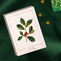 Card with holly leaf and berry illustration on a green fabric background
