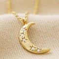 Gold crescent moon necklace with embedded stones on a beige fabric background