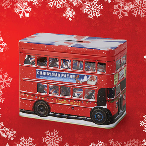A red double-decker bus-shaped Christmas tin with snowflake details, featuring a 'Christmas Patter' advertisement on the side, set against a red background with white snowflakes.