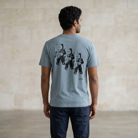 Man wearing a light blue t-shirt with a graphic design of three astronauts on the back, standing against a plain wall.