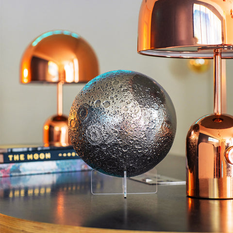 Decorative moon sphere on a stand with two copper lamps in the background.
