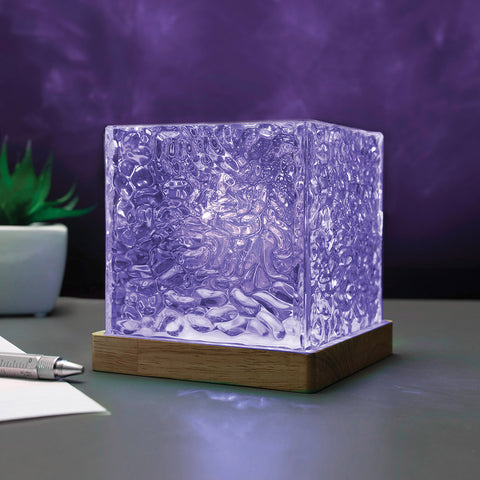 Cube-shaped light with wooden base on a table against a dark background
