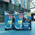 Book titled 'The Ocean Map' by Aimee Mook on a blue floor with a building in the background