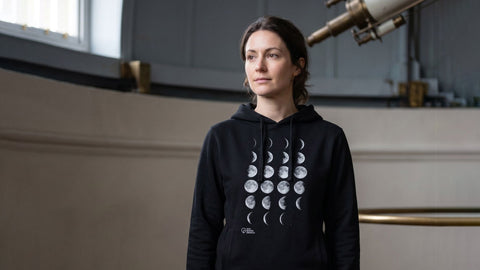 Person wearing a black hoodie with moon phase design in an observatory setting
