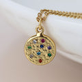 Gold necklace with a round pendant featuring colorful gemstones on a light background