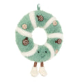 A plush Christmas wreath ornament in mint green and white faux fur, decorated with brown pinecones and small beige ornaments, featuring a smiling face and dangling legs.
