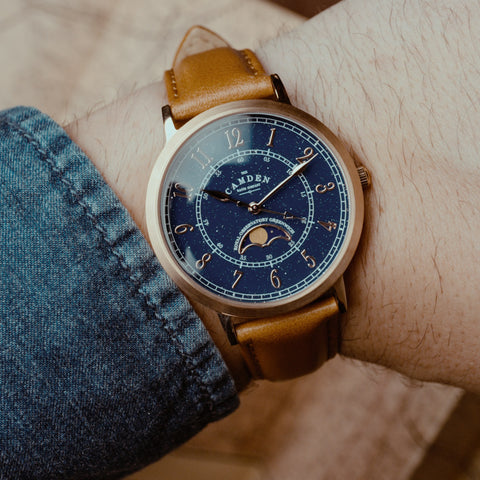 Rose-gold watch with blue face and tan leather strap on a wrist.