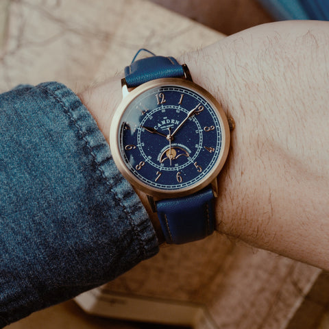 Rose-gold watch with blue face and blue leather strap on a wrist.