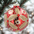 Decorative red and gold Christmas ornament on a tree branch with blurred lights in the background