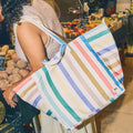 Person holding a colourful striped tote bag in a market setting