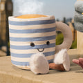 Striped mug plush toy with a face and pom-pom details on a wooden surface