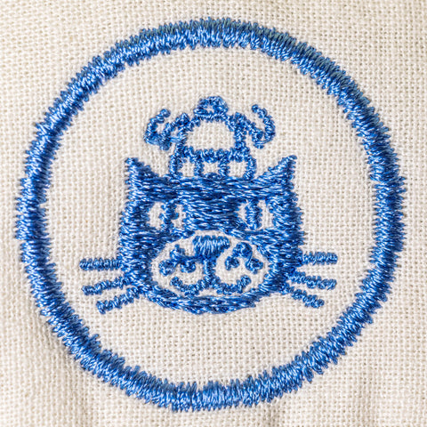 Embroidered design of a cat with a blue border on beige fabric