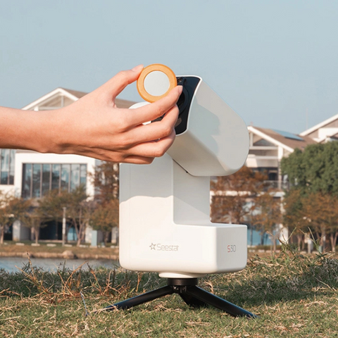 Hand attaching magnetic solar filter on front view of Seestar S30 astrophotography telescope set against an outdoors backyard backdrop