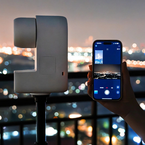 Seestar S30 astrophotography telescope back view set on a tripod looking out over a cityscape. Hand holding a smartphone showing app connection next to product.