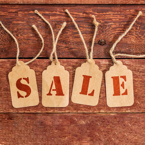 Four brown paper tags with red letters spelling 'SALE' on a wooden background