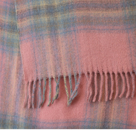 A close-up of a soft plaid scarf in dusty pink with blue and yellow stripes, finished with fringed edges.