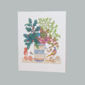 A white greeting card featuring a colorful illustration of a floral arrangement in a patterned vase, with a pheasant, squirrel, and small birds, shown against a solid gray background.