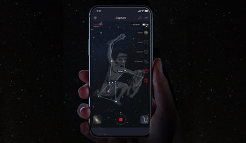 Hand holding a smartphone with a stargazing app displaying a zodiac sign against a starry night background.