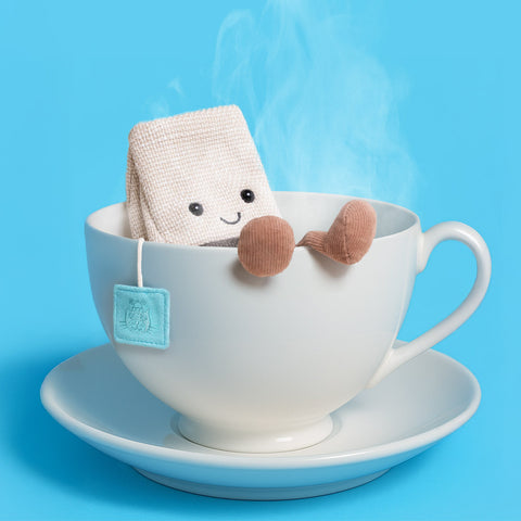 Plush teabag toy with a smiling face inside a white teacup on a blue background