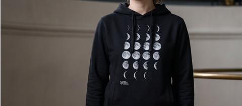 Person wearing a black hoodie with moon phase design on a neutral background