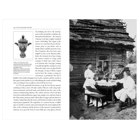 A black and white image of people wearing bonnets and hats, sitting at a table drinking tea in front of a log built building.
